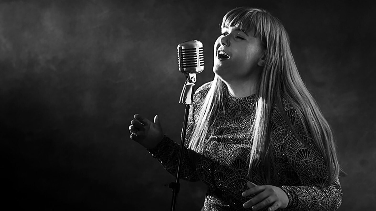 woman singing into a vintage microphone with long hair and dramatic lighting in black and white